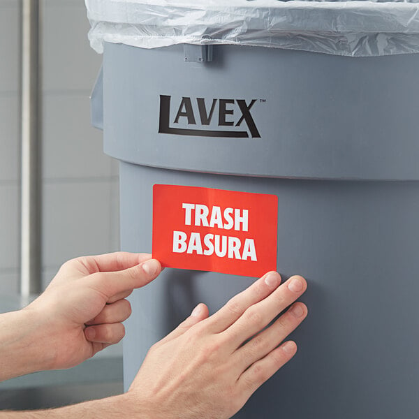 A person's hands putting a Lavex Waste Stream label on a trash can.