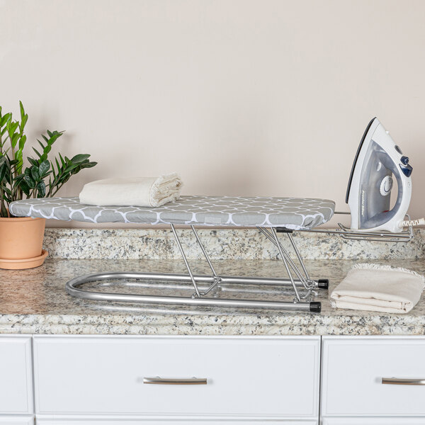 A Household Essentials steel mesh ironing board on a table with a trellis cover.