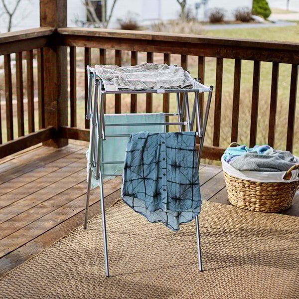 A silver Household Essentials collapsible steel drying rack holding a blue shirt with black squares on a porch.