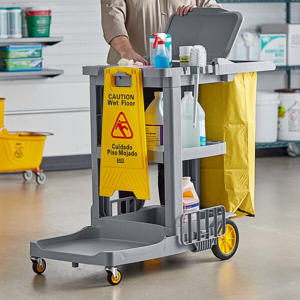 A man holding a Lavex Premium yellow 3-shelf janitor cart.