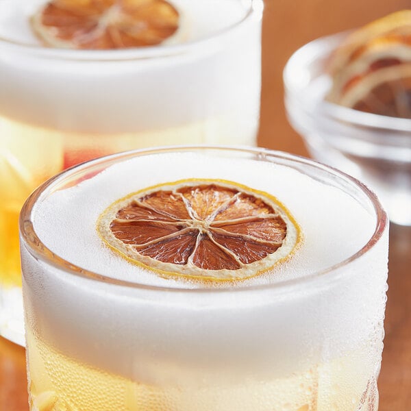 A close-up of a cup of orange juice with a dried lemon slice.