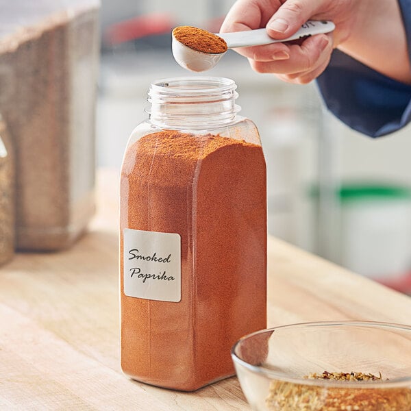 A person pouring spice into a rectangular plastic spice container.