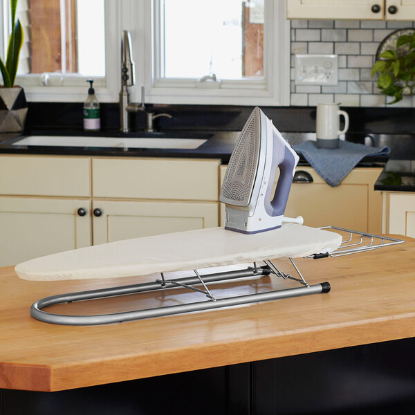 A Household Essentials steel mesh ironing board with a white cover and iron rest with an iron on it.