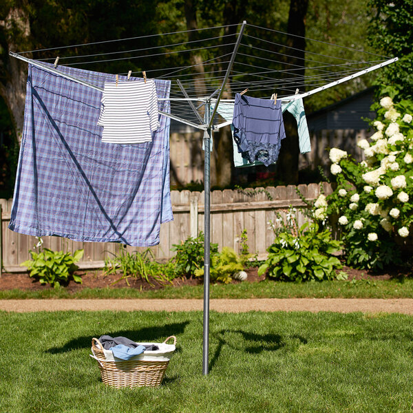 A Household Essentials rotary clothes line with a white shirt, striped shirt, and plaid sheet drying on it.