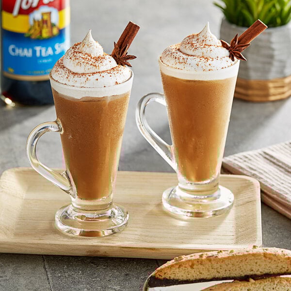 Two glasses of brown liquid with whipped cream and cinnamon sticks with Torani Chai Tea Spice flavoring.