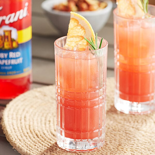 A glass of Torani grapefruit flavored liquid with a slice of orange on the rim.