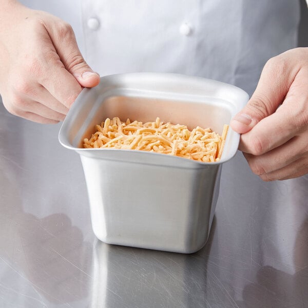 A person holding a Vollrath stainless steel food pan filled with noodles.