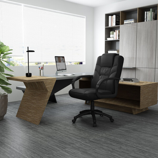 A black Boss LeatherPlus high-back office chair with wheels at a desk in a room.