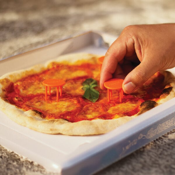 A hand placing small plastic chairs on a pizza in a GI Metal plastic pizza box.
