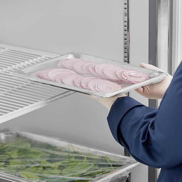 A person holding a Vollrath stainless steel steam table pan filled with food.