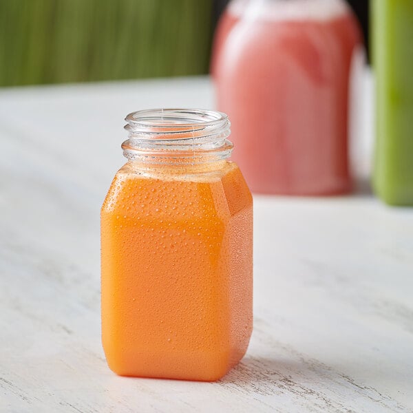 A customizable square PET clear energy juice bottle on a table with two other juice bottles.