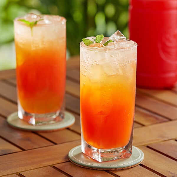 Two glasses of Finest Call Tropical Puree with ice on a table in a cocktail bar.