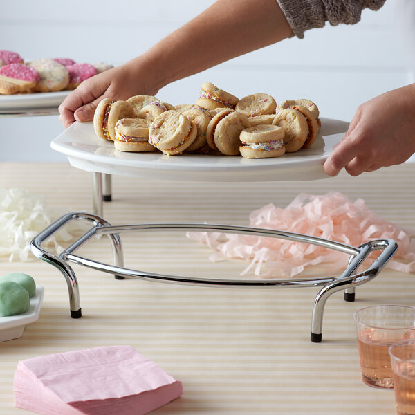 A person holding a plate of cookies using a Vollrath 3" Display Stand.