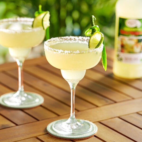Two glasses of Master of Mixes Spicy Margarita Mix garnished with lime and salt on a wooden table.