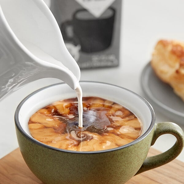 A pitcher pouring Oatly Oat Milk Half and Half into a cup of coffee.