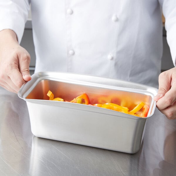 A person holding a Vollrath stainless steel rectangular food pan with peppers inside.