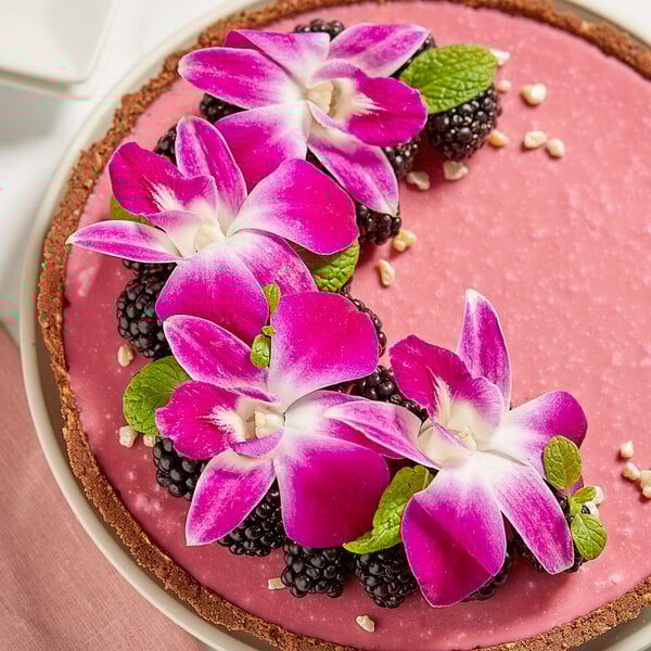 A pink cake with purple orchids on top.