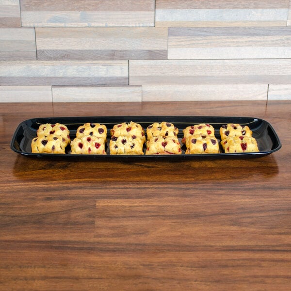 A black Sabert plastic catering tray holding a group of baked goods on a table in a bakery.