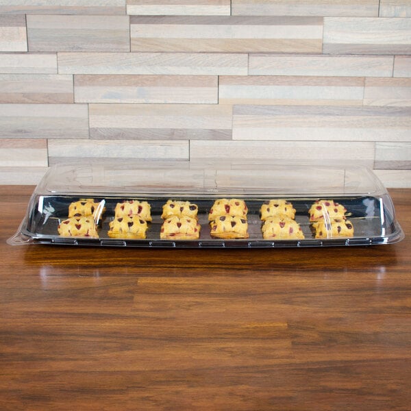 A Sabert Mozaik black plastic catering tray holding a group of pastries on a table.