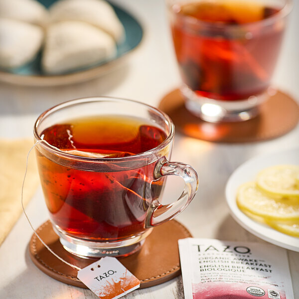 A glass cup of Tazo Organic Awake English Breakfast tea with a tea bag on a coaster.