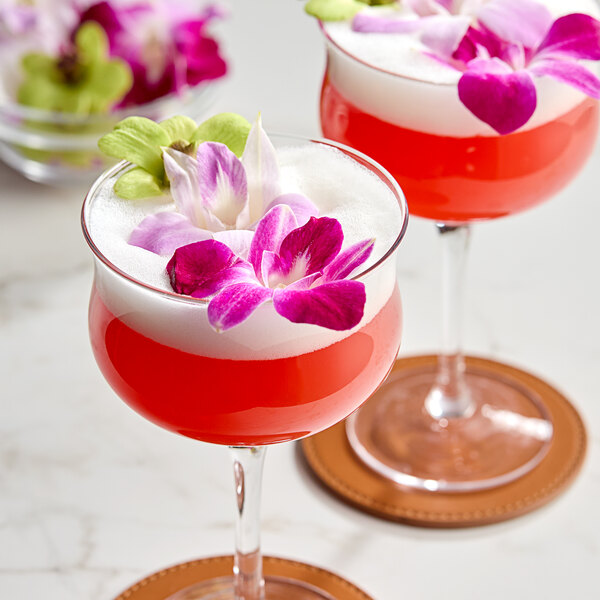A drink in a glass with a pink drink and a Mixed Color Orchid on top.