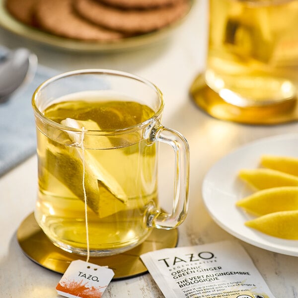 A glass mug of Tazo Organic Green Ginger Tea with a tea bag in it.