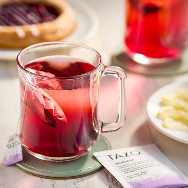 A glass mug with a Tazo Passion tea bag steeping in red liquid.