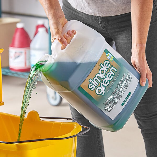 A person pouring Simple Green Sassafras scented industrial cleaner from a white jug into a yellow bucket.