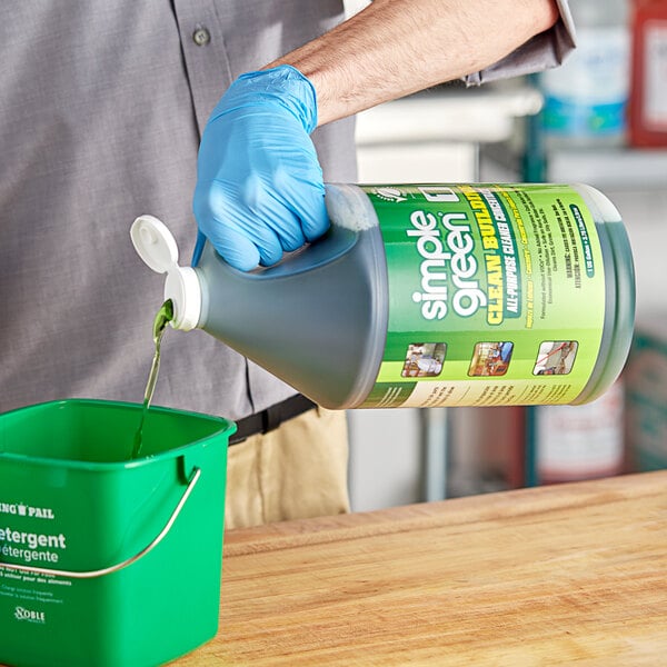 A person wearing blue gloves pouring green Simple Green liquid into a bucket.