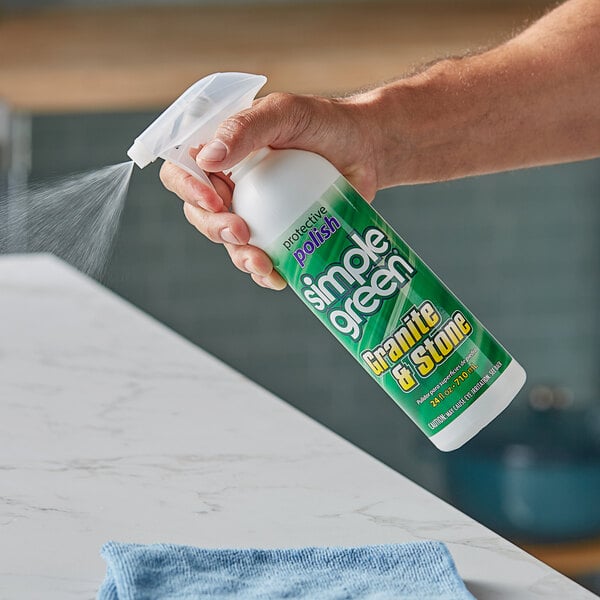 A hand spraying Simple Green granite and stone polish from a white and green bottle on a kitchen counter.