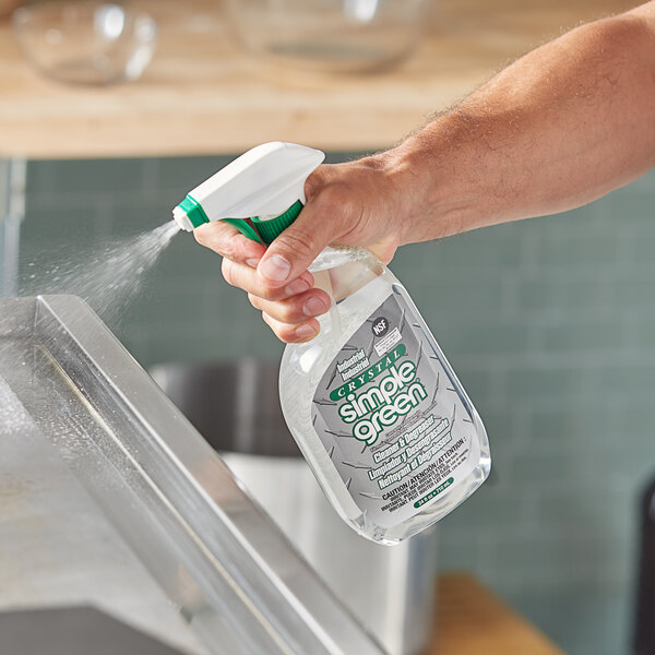 A hand holding a Simple Green spray bottle and spraying liquid onto a metal surface.