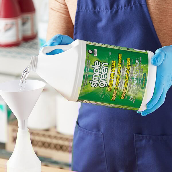 A person in blue gloves pouring Simple Green liquid into a white container with a green label.