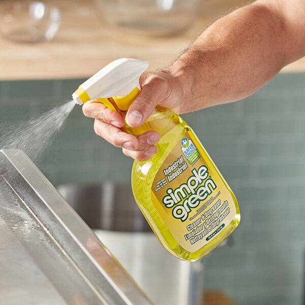 A hand using Simple Green Lemon Scent cleaner to spray a kitchen counter.