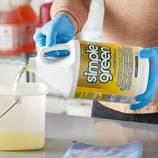 A person in blue gloves pouring Simple Green Lemon Scent Concentrated Industrial Cleaner into a container.