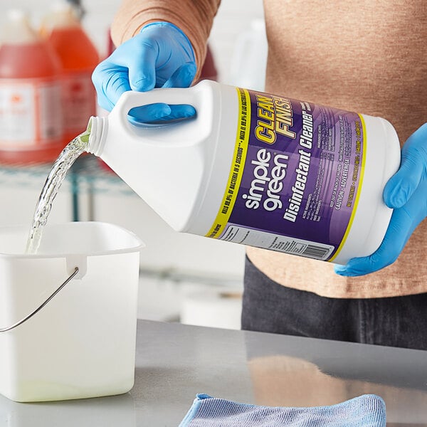 A person in blue gloves pouring Simple Green Mint Scented Disinfectant Cleaner from a jug into a white bucket.