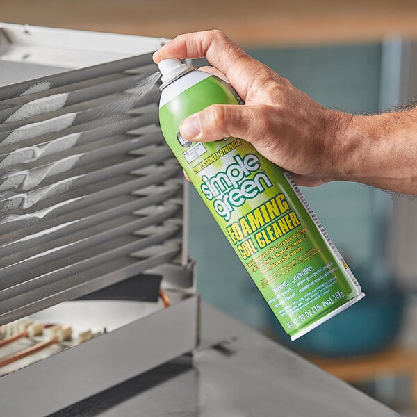 A hand holding a green can of Simple Green foaming coil cleaner with white text.