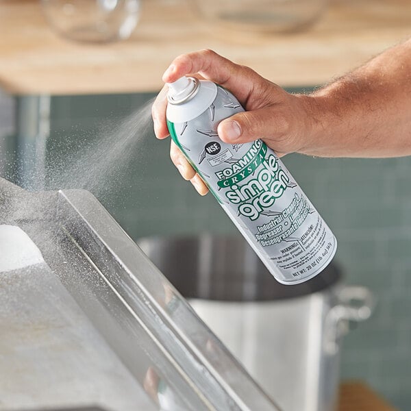 A hand holding a Simple Green Crystal spray can spraying a kitchen counter.