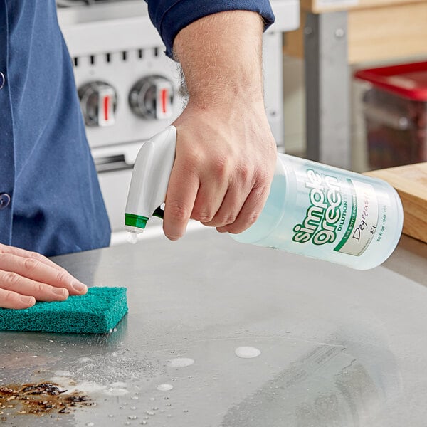 A hand holding a Simple Green plastic spray bottle and spraying a surface.