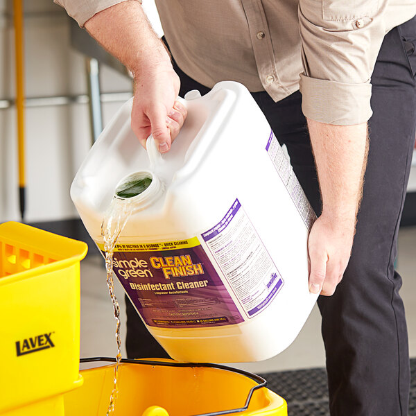 A person pouring mint green liquid from a jug into a bucket.