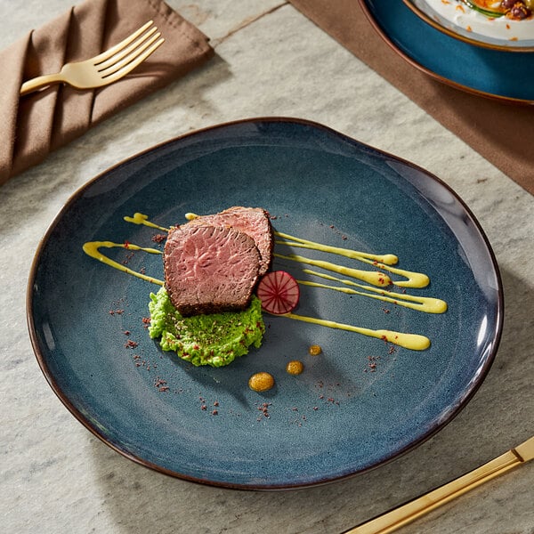 An Acopa Highlands Skyfall Blue coupe china plate with a piece of meat on it on a table.