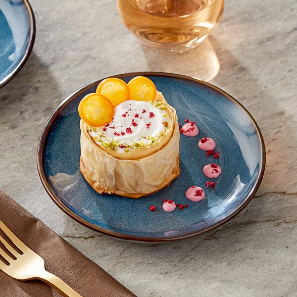 An Acopa Highlands blue coupe china plate with a dessert and a gold fork on a brown napkin.