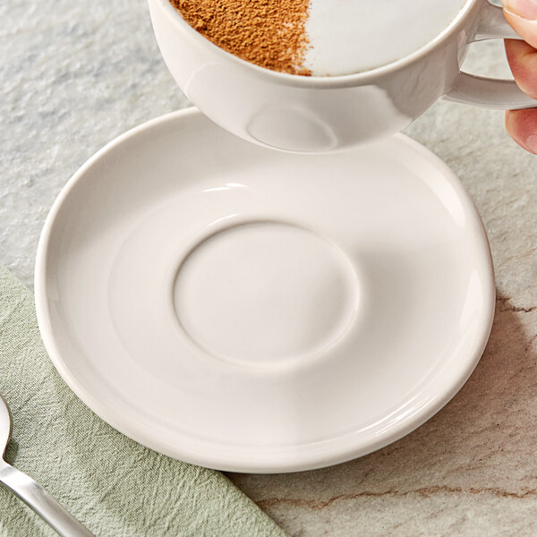 A hand pouring coffee into a white Acopa birch saucer with a white cup on it.