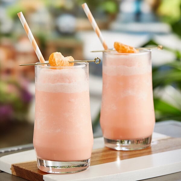 Two glasses of Tiki Breeze Super Blend pink smoothies with straws and orange slices.