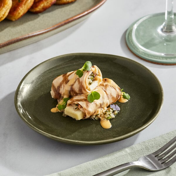 A plate of food on an Acopa Highlands Juniper Green China plate with a fork and a glass of wine.