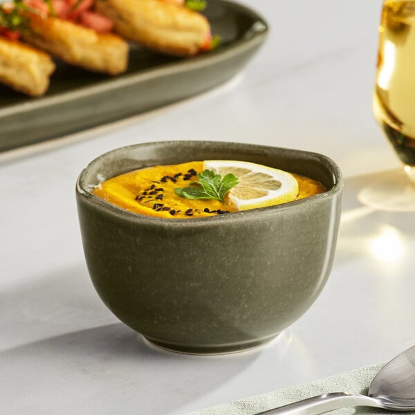 An Acopa Highlands juniper green bouillon cup filled with soup and garnished with a lemon slice and herbs.