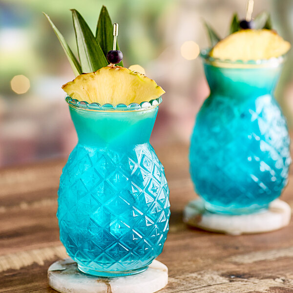 A blue drink in a Tiki glass with a pineapple garnish and a blue umbrella.