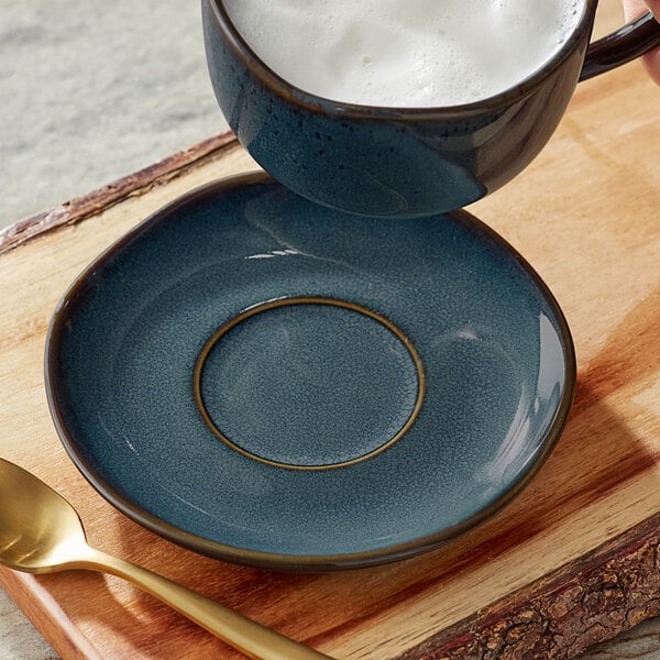 A cup of coffee with foam on a Acopa Highlands skyfall blue saucer.