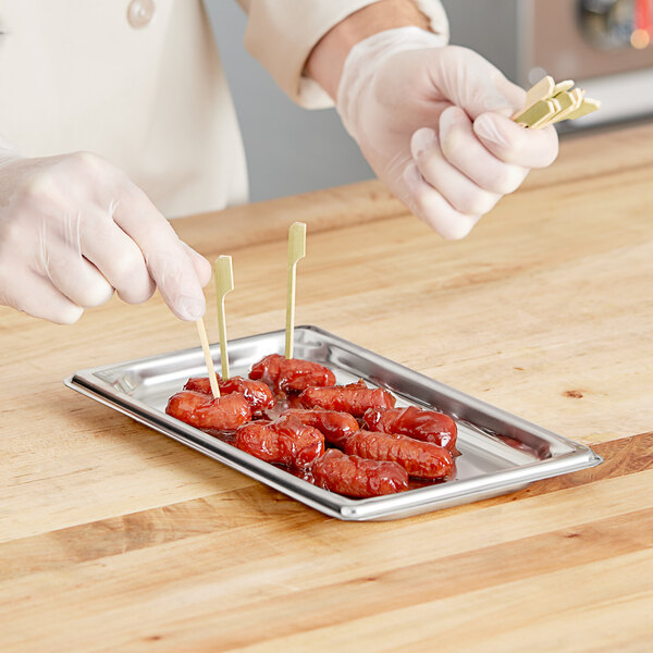 A person holding a Vollrath stainless steel steam table pan filled with food.