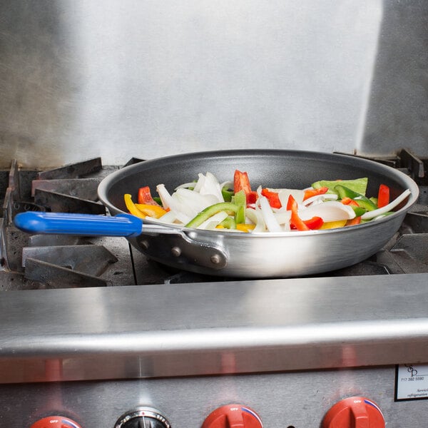 A Vollrath Wear-Ever aluminum non-stick fry pan with vegetables cooking on a stove.