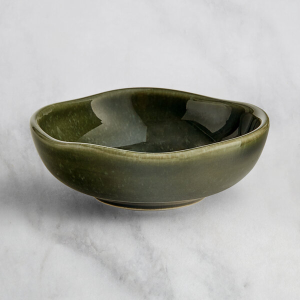 An Acopa Highlands juniper green sauce cup on a marble surface.